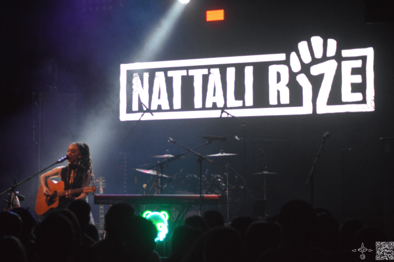 Nattali Rize on stage performing with a guitar and drums

