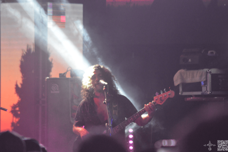The bass player, Patricio Zuñiga Labarca, standing and playing the bass in a beam of light, A scanable code logo in the bottom right corner
