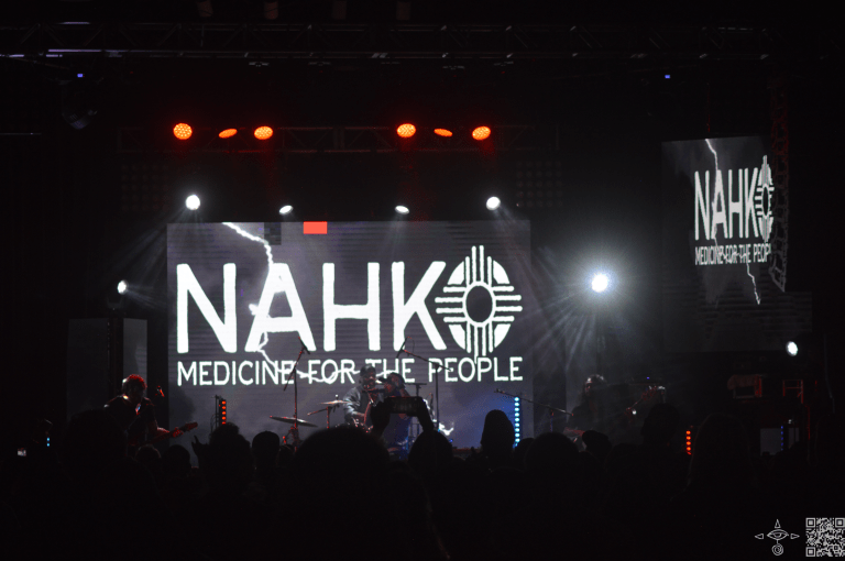 Nahko on stage, zoomed out perspective, Lighting, red lights and black surrounding 