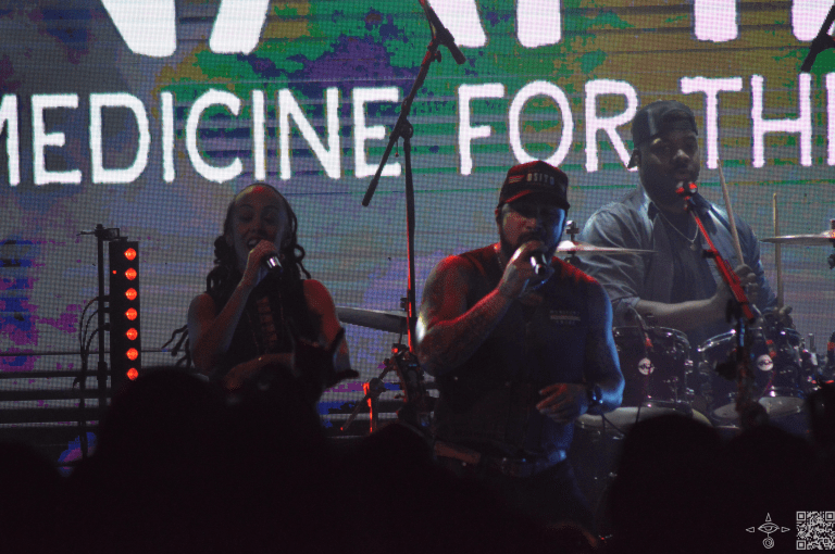 Nahko on stage with Nattali Rize and the Drummer Justin Chittams, closer perspective, a dark shot.